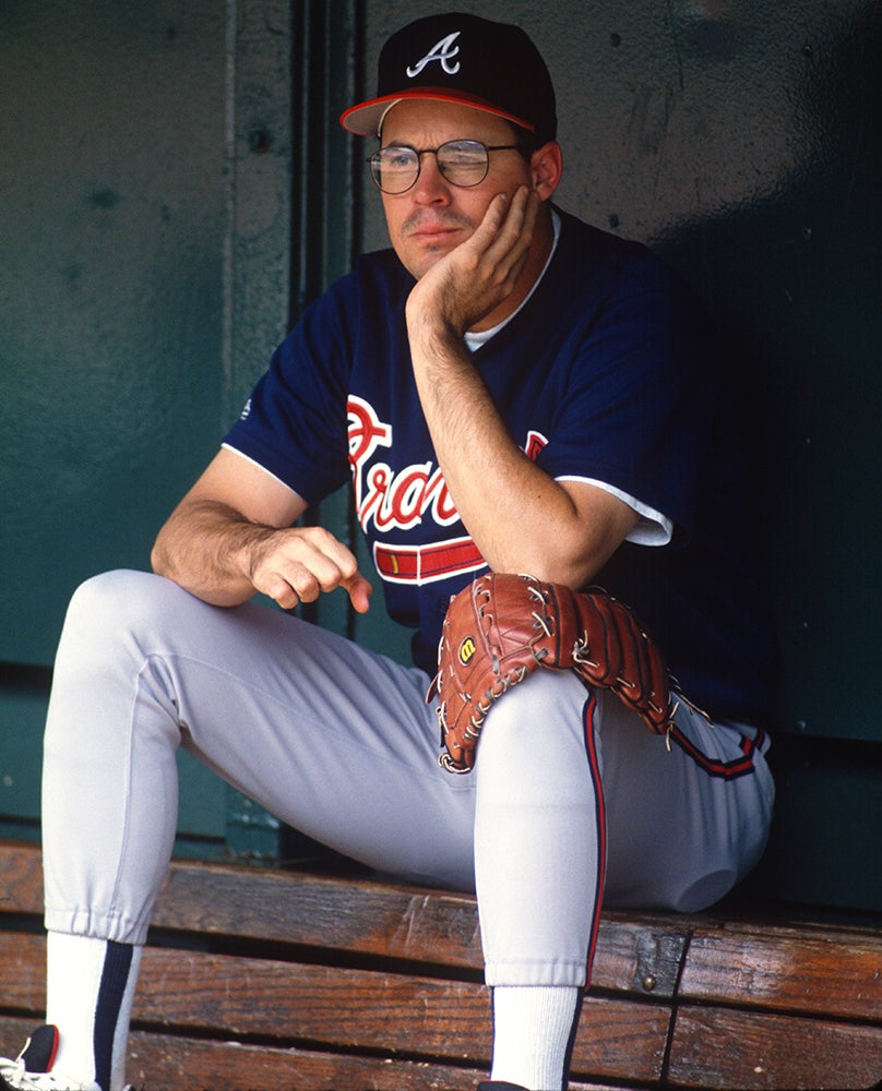 Greg Maddux sits in dugout wearing Braves jersey